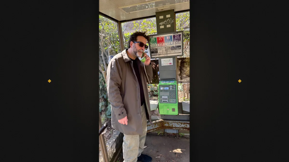 Ugo Esposito, fondatore di Kapusons, al telefono in una cabina telefonica giapponese — composizione su fondo scuro con accenti oro