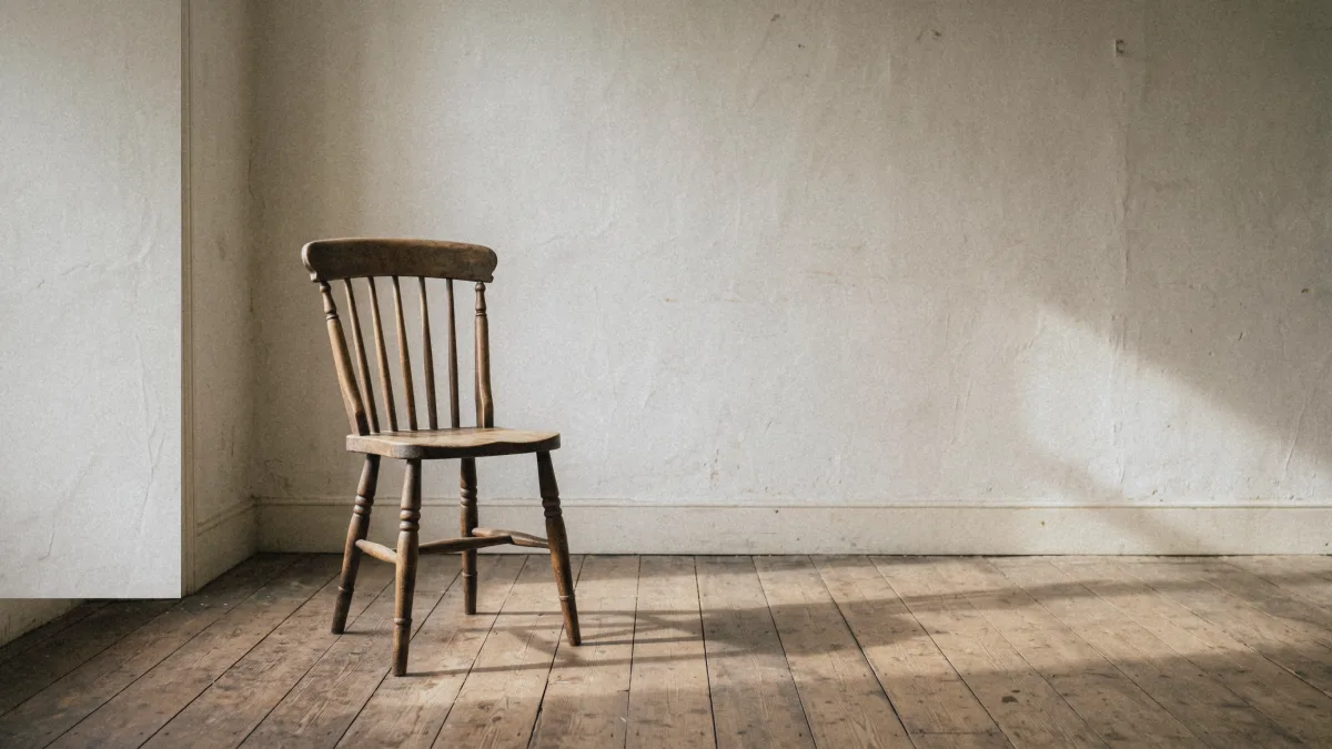 Sedia di legno semplice in una stanza spoglia con pavimento di assi, illuminata dalla luce calda del mattino