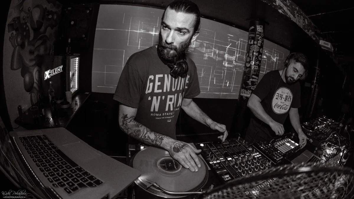 DJ Drugo alla console durante un live, mano sul vinile (foto: Klárka Pohanková)