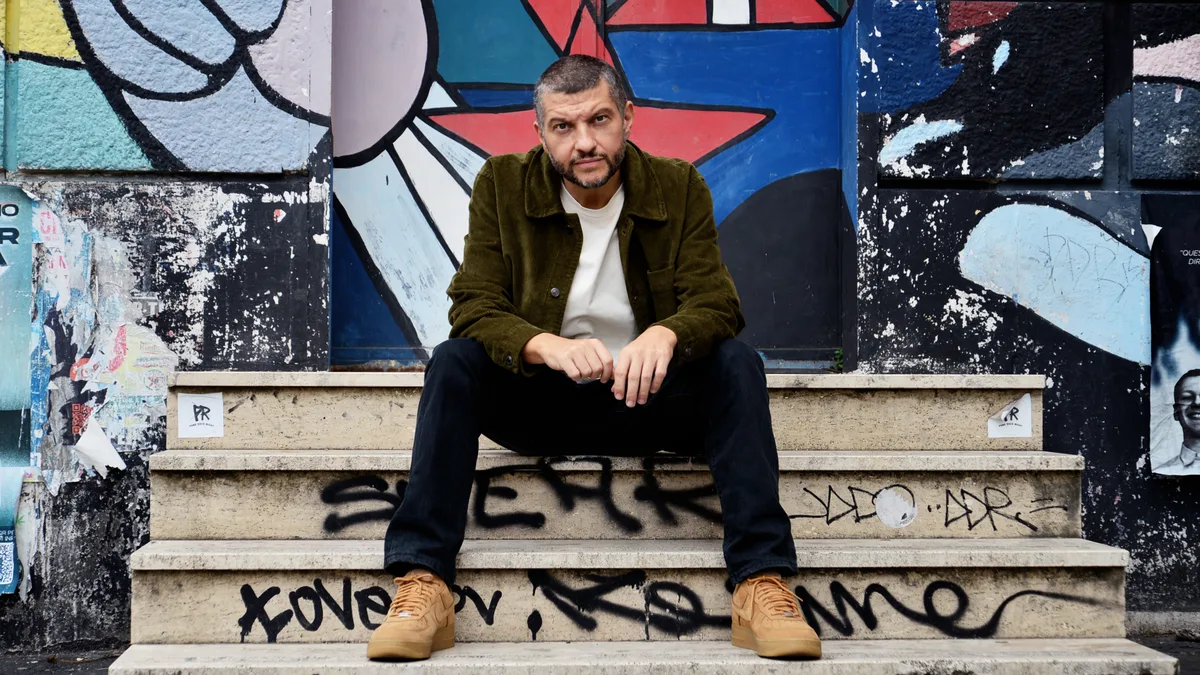Il rapper Francesco "Kento" Carlo seduto sui gradini di una scalinata davanti a un murale colorato